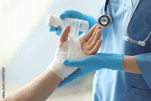 Fototapeta Medical assistant applying bandage onto patient's hand in clinic, closeup