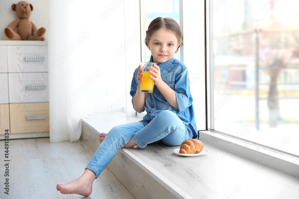 Cute little girl having breakfast while sitting on window sill at home Cute little girl having breakfast while sitting on window sill at home