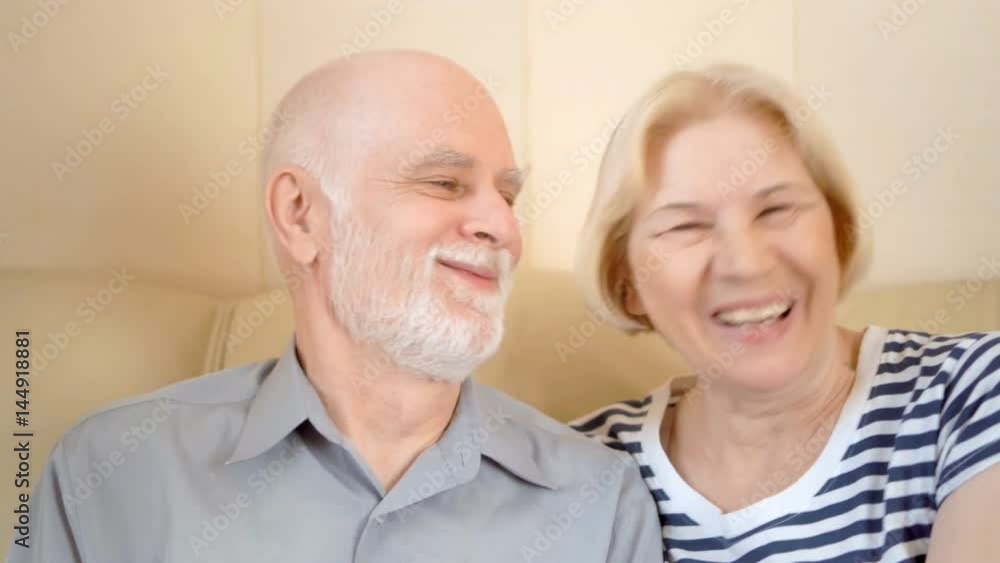 Cheerful good-looking senior couple sitting on sofa at home. Kissing smiling having good time. Cheerful good-looking senior couple sitting on sofa at home. Kissing smiling having good time.