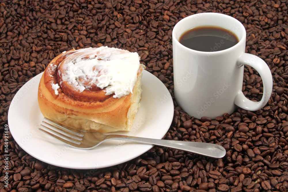 A white coffee cup with a pastry on a plat with fork on a background of coffee beans A white coffee cup with a pastry on a plat with fork on a background of coffee beans