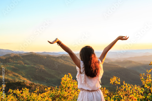 Asian teenage girl Asia ethnic cheerful front is a flower and overlooks the mountain complex and sky at sunset or sunrise on the mountain with copy space.