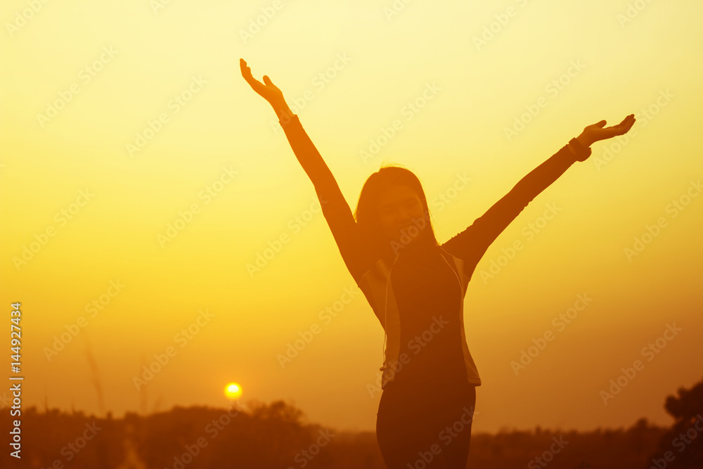 Happy woman raised hands up on the sky at sunset
