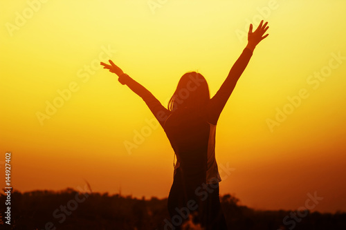 Happy woman raised hands up on the sky at sunset