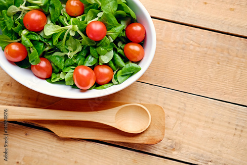 Cherry tomatoes and basil salad in a white cup on a wooden table.