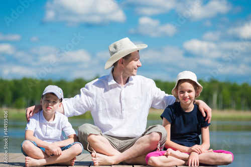 father with daughter and son sits on a beautiful pier on the lake © kurgu128