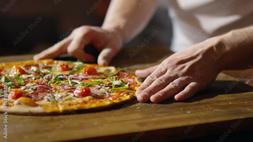 Tracking shot of male hands sliding freshly baked delicious pizza from wooden board to serving plate Tracking shot of male hands sliding freshly baked delicious pizza from wooden board to serving plate