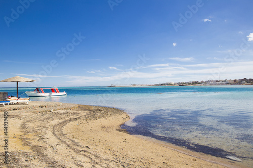 Sea beach with vacationers and a pleasure boat at the shore against the blue sky photo