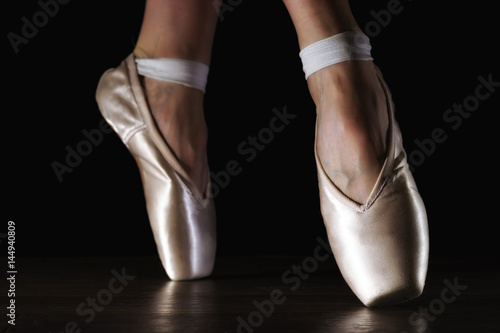 Close-up classic ballerina's legs in pointes on the black floor