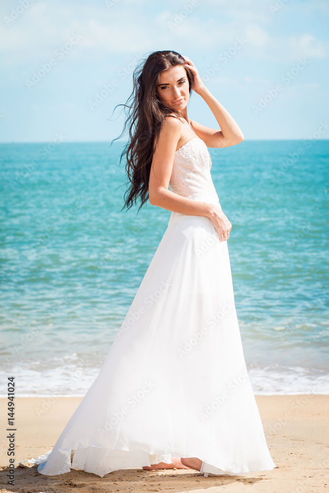 Fashion bride walking down the sea coast in a white dress. Beautiful girl walks barefoot down the beach. Fashion bride walking down the sea coast in a white dress. Beautiful girl walks barefoot down the beach.