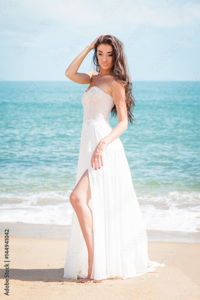 Fashion bride walking down the beach in a white dress. Beautiful girl walks barefoot down the beach. Fashion bride walking down the beach in a white dress. Beautiful girl walks barefoot down the beach.