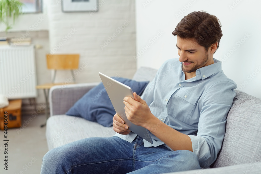 mann sitzt auf dem sofa und schaut auf sein tablet mann sitzt auf dem sofa und schaut auf sein tablet