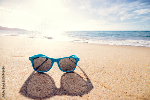 Vacation concept. Blue sunglasses on the sea beach sand.