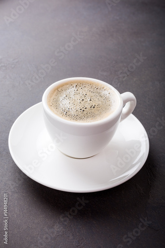 White cup of coffee on dark brown background with copy space.