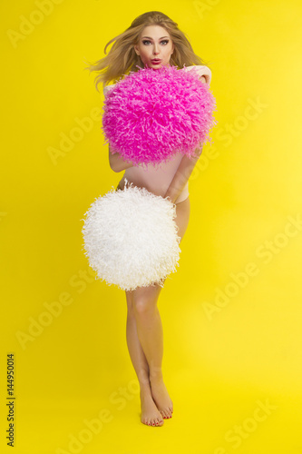 Blond girl cheering with pom pom, yellow background photo