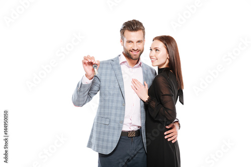 Happy young loving couple standing isolated holding keys.