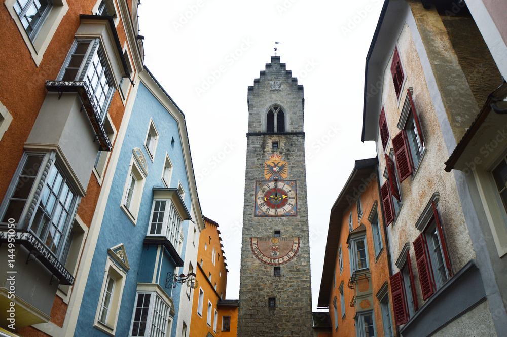 VIPITENO, ITALY - NOVEMBER 23, 2016: Medieval tower clock with colorful houses in Via Città Nuova, center of Vipiteno, historic village classified among the most beautiful in Italy, South Tyrol, Italy