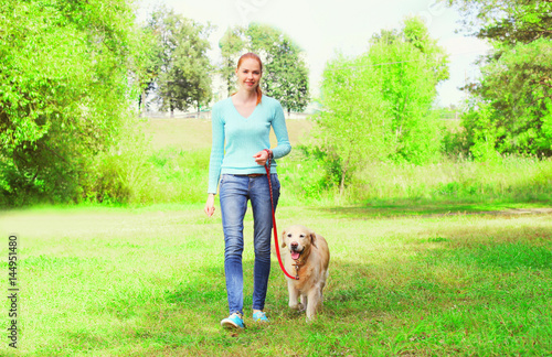 Happy owner woman with Golden Retriever dog is walking together in a spring park