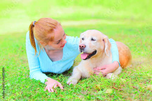 Happy smiling owner woman and Golden Retriever dog is lying on the grass