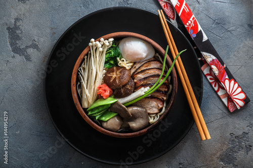 Ramen noodles with duck, egg, enoki and shiitake mushrooms with broth on dark background photo