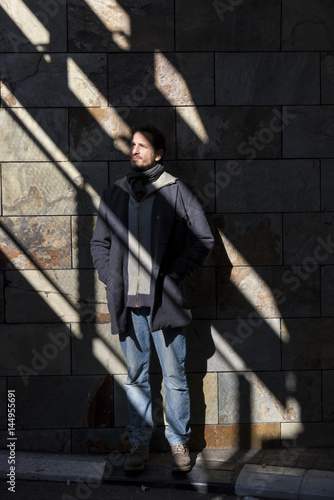 Young man poses illuminated by the rays of the sun in the shade