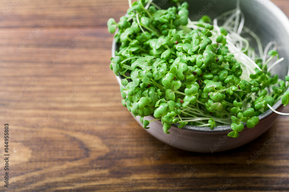 Mustard microgreen salad in metallic bowl on wooden background Mustard microgreen salad in metallic bowl on wooden background