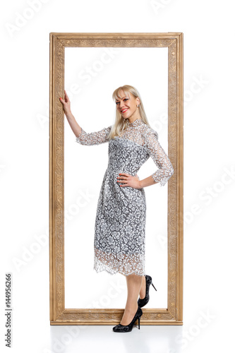 Pretty blonde girl standing inside big picture frame isolated on white