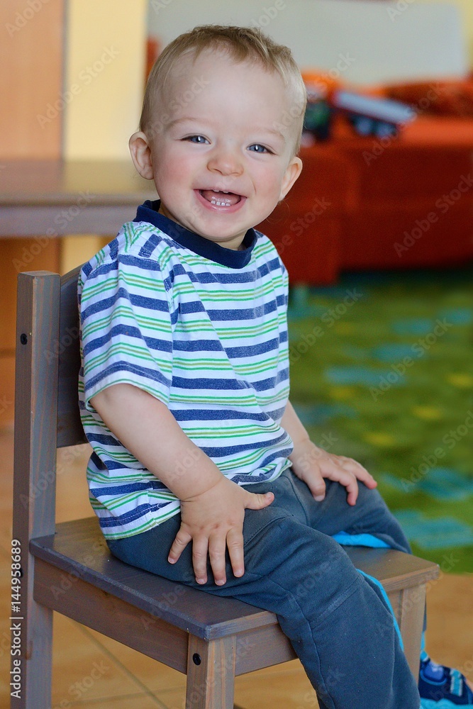 Happy boy sitting on his first small wooden chair. Child concept. Happy boy sitting on his first small wooden chair. Child concept.