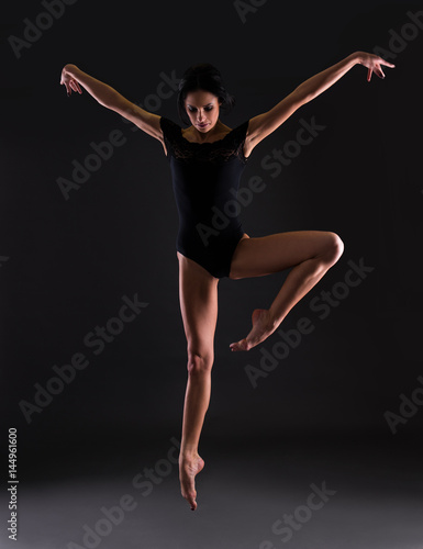 beautiful woman ballerina in black body suit jumping over black © Di Studio