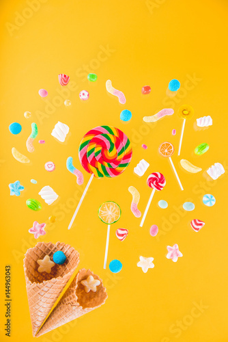 Close-up top view of waffle cones and mix of various sweets on yellow background