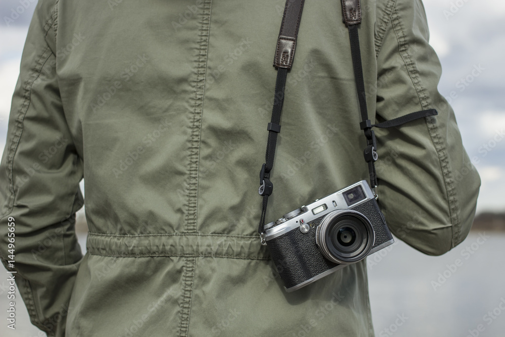 Old camera hanging on the shoulder of a person against a cloudy sky background Old camera hanging on the shoulder of a person against a cloudy sky background