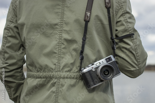 Old camera hanging on the shoulder of a person against a cloudy sky background