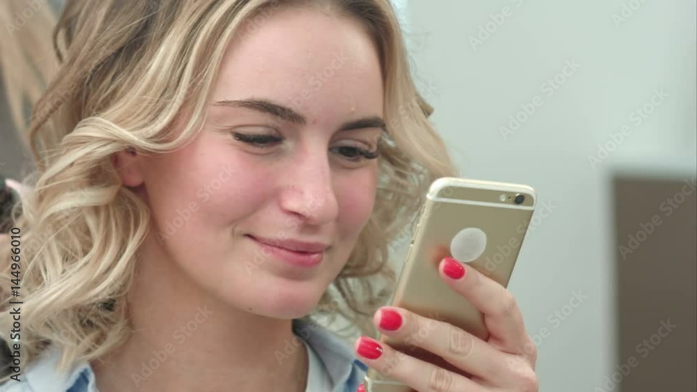 Beautiful woman using smartphone in a beauty salon, while having a hair styling Beautiful woman using smartphone in a beauty salon, while having a hair styling