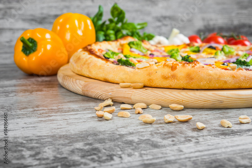 Vegetarian pizza with rosemary and spices on a light wooden background. Italian pizza on a background of green basil and fresh vegetables