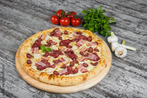 Pizza with smoked meat, with rosemary and spices on a light wooden background. Italian pizza on a background of green basil and fresh vegetables