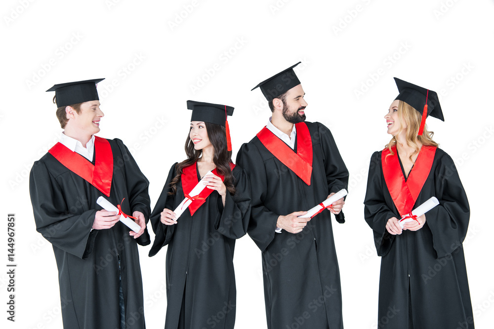 Group of young men and women in graduation gowns and mortarboards holding diplomas Group of young men and women in graduation gowns and mortarboards holding diplomas