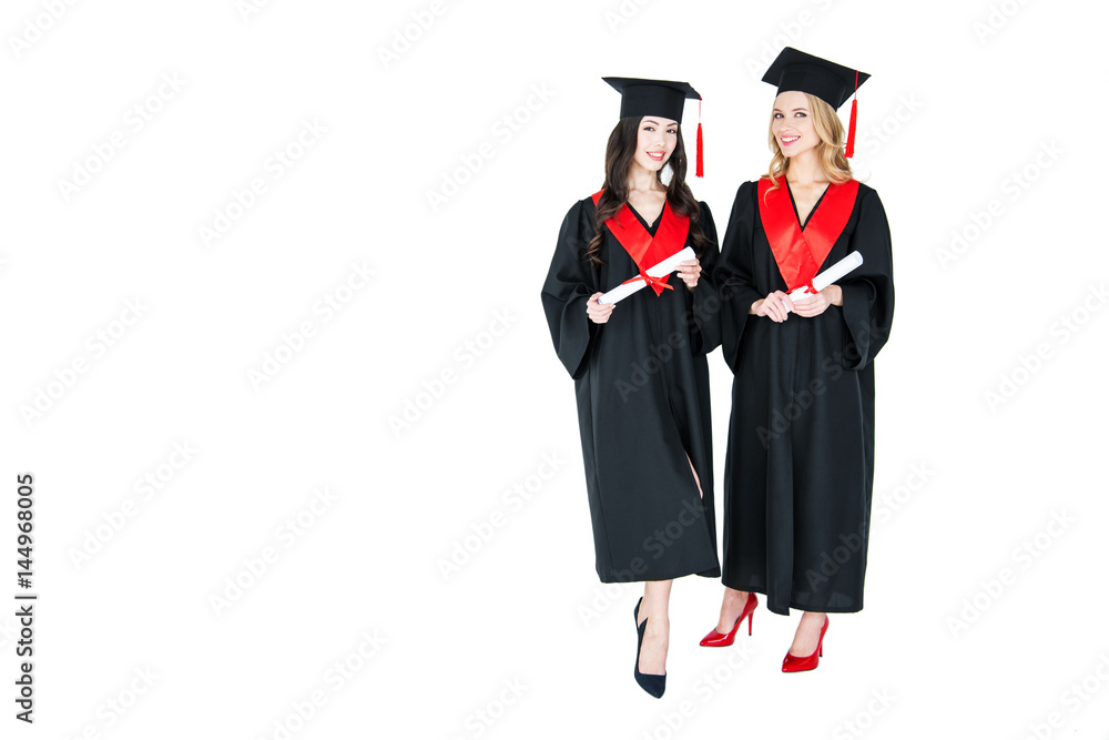 Two happy young women in academic gowns and mortarboards holding diplomas Two happy young women in academic gowns and mortarboards holding diplomas