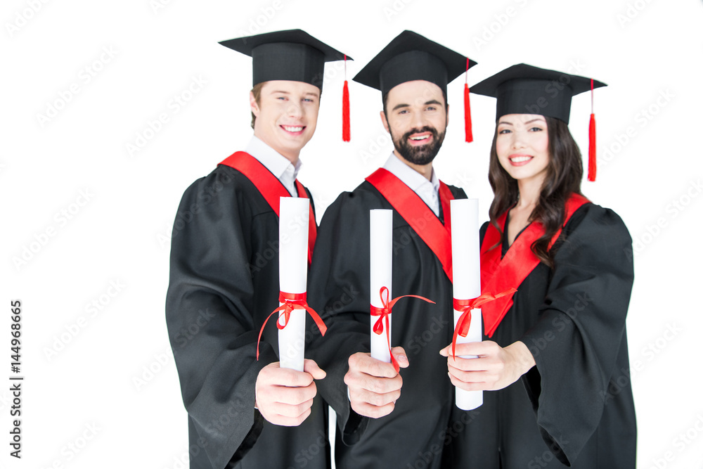Happy students in graduation caps holding diplomas and smiling at camera Happy students in graduation caps holding diplomas and smiling at camera