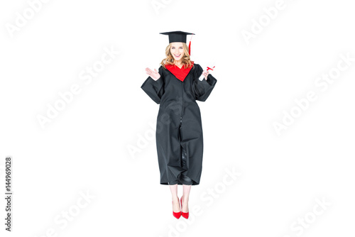 attractive student in graduation cap with diploma jumping isolated on white