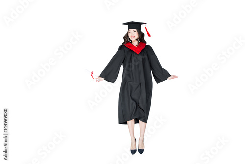 attractive student in graduation cap with diploma jumping isolated on white