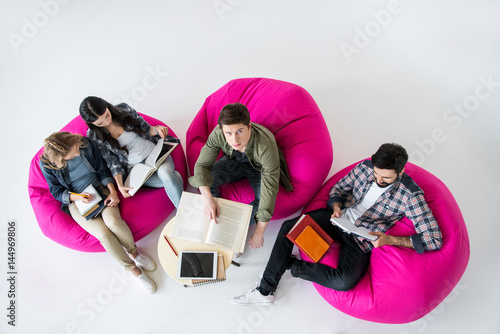 overhead view of students sitting on beanbag chairs and studying in studio on white
