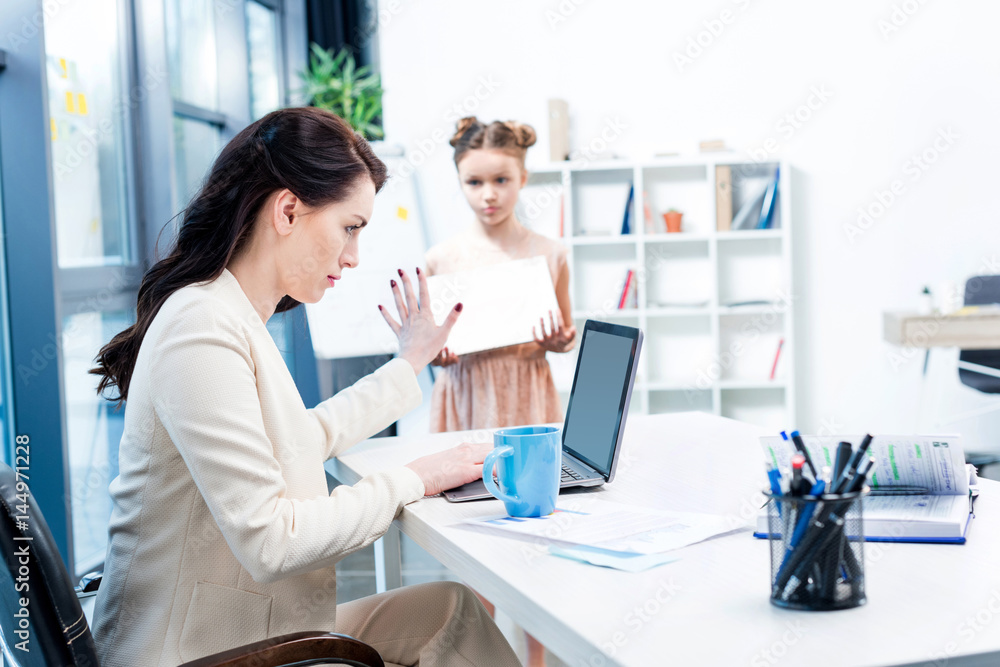busy businesswoman showing stop sign to her daughter with drawing album in office busy businesswoman showing stop sign to her daughter with drawing album in office