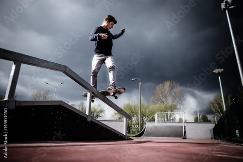 Skater doing boardslide trick on rail in skatepark during stormy dramatic weather 