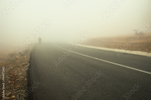 Distant silhouette of a man approaching on the side of the highway through the thick fog