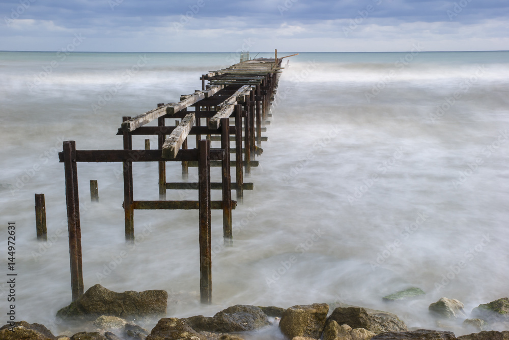 Deserted pier on the Bulgarian Black Sea shore under an agitated water and approaching storm Deserted pier on the Bulgarian Black Sea shore under an agitated water and approaching storm