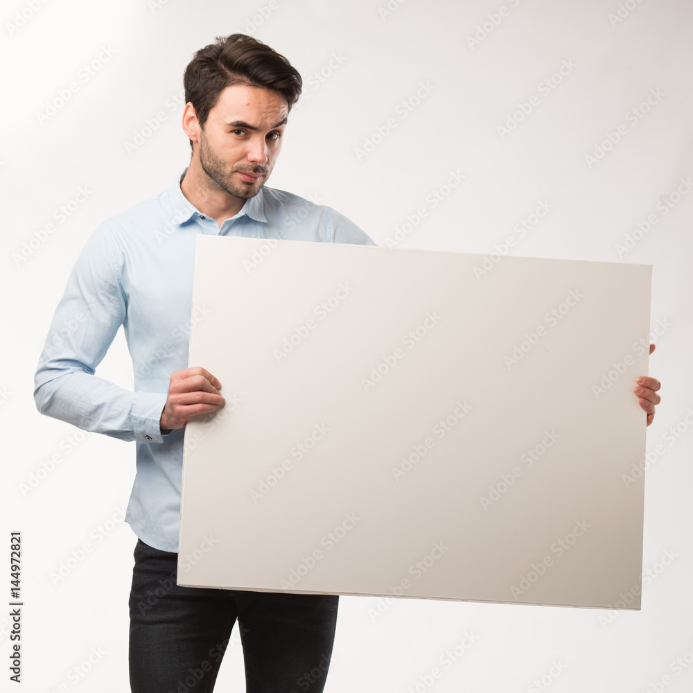 Young happy man showing presentation, pointing on placard over gray background Young happy man showing presentation, pointing on placard over gray background