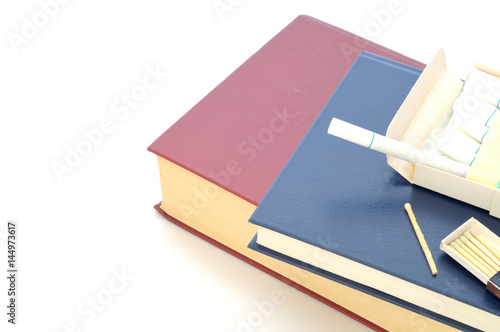 Cigarette and matches over a stack of books, white background