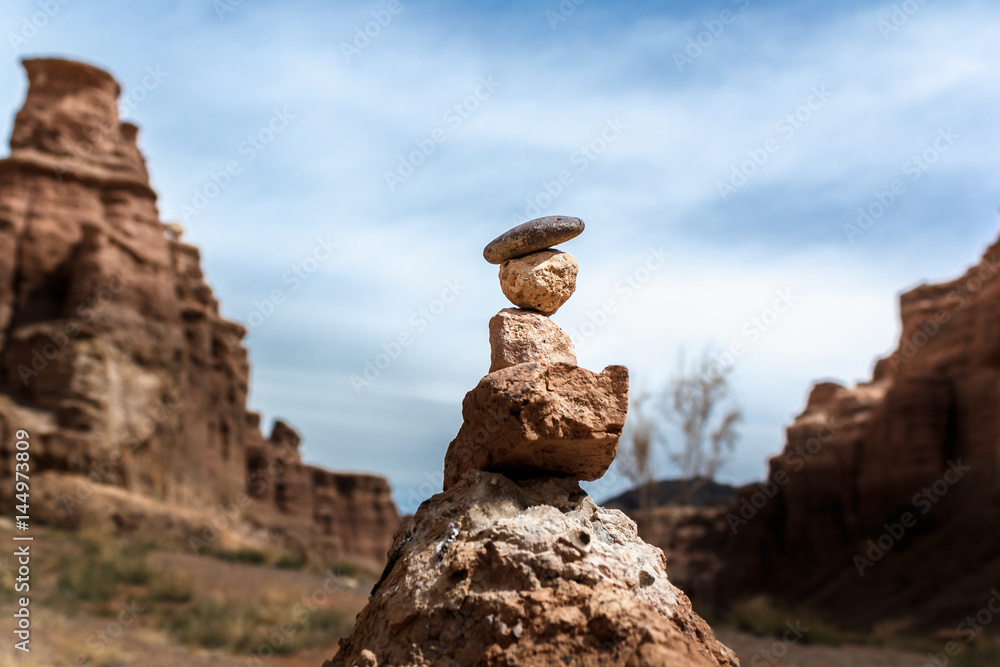 Stone totem on a background of red rocks and sky with clouds