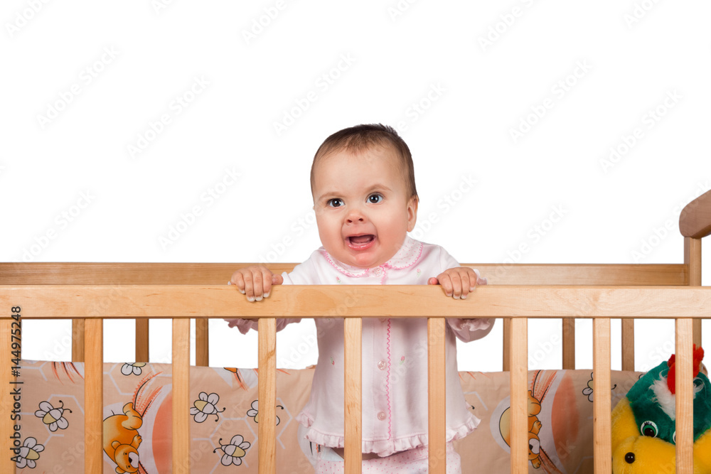 Sad Infant child baby girl toddler in wooden bed on white background Sad Infant child baby girl toddler in wooden bed on white background
