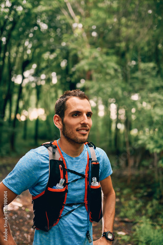 Fit male jogger rests during day jogging for cross country forest trail race in a nature park.