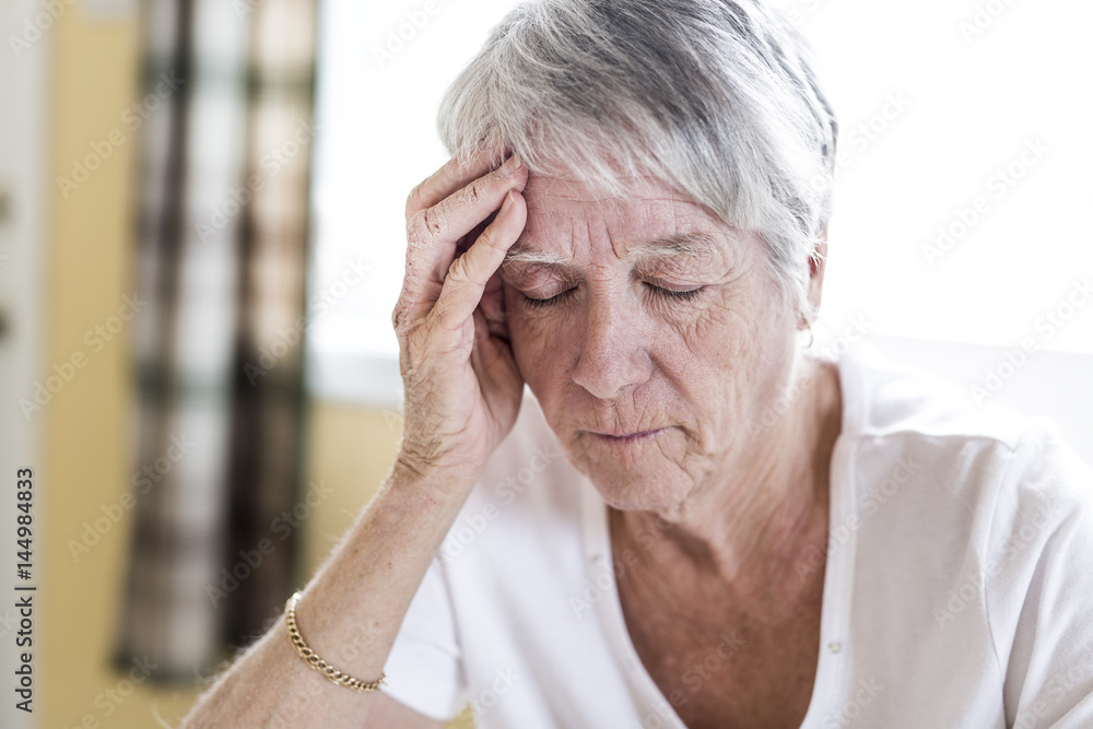 Mature woman at home touching her head with her hands while having a headache pain
